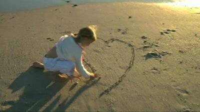 Girl drawing heart in sand