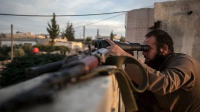 A Syrian opposition fighter watches over as heavy fighting sparks out in the neighbouring village of Kafr Nabuda