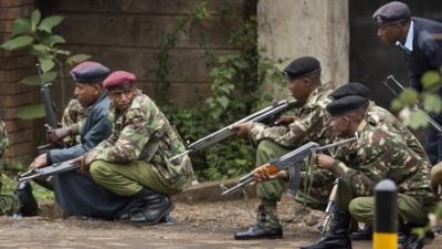 Armed police from the General Service Unit take cover behind a wall during a bout of gunfire, outside the Westgate Mall in Nairobi