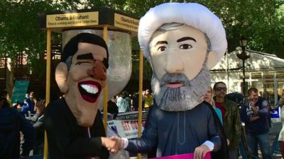 Men wearing masks of Presidents Obama and Rouhani, shaking hands