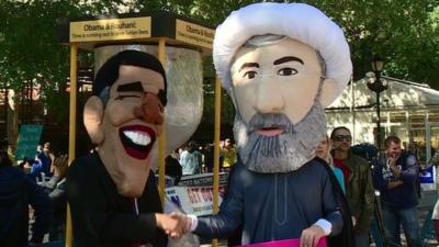 Men wearing masks of Presidents Obama and Rouhani, shaking hands