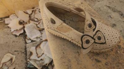 A child's shoe and burnt papers and books on the ground.