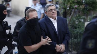 Far-right Golden Dawn party leader Nikos Mihaloliakos (R) is escorted by anti-terrorism police officers as he arrives at a courthouse in Athens