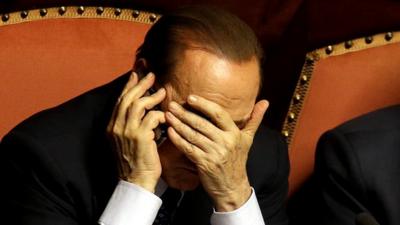 Silvio Berlusconi covers his face as he speaks on a mobile phone after delivering his speech at the Senate in Rome