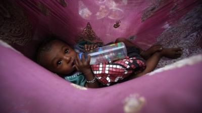Shankar, a six-month-old homeless boy, drinks milk from a bottle as his parents eat their lunch at a street in Mumbai
