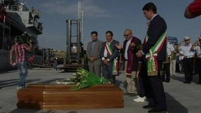 Officials stand in front of coffins in Sicily