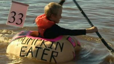 Child rowing inside a giant pumpkin on a lake