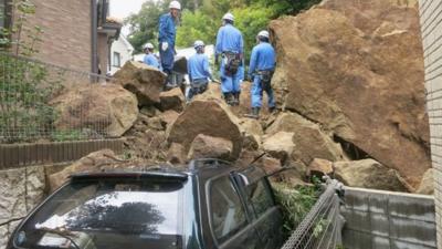 Fire fighters stand on rocks fallen from a cliff over a garage and a road in a residential area in Kamakura, southwest of Tokyo