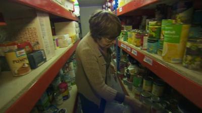 Food bank worker collecting and bagging tins of food