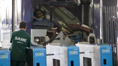 Police officers and paramedics inspects a commuter train that slammed into the buffers at the end of the line when arriving at Once central station in Buenos Aires