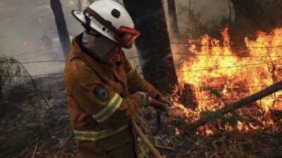 A Rural Fire Service fire-fighter sprays water onto a small fire burning near a home in the Blue Mountains suburb of Faulconbridge