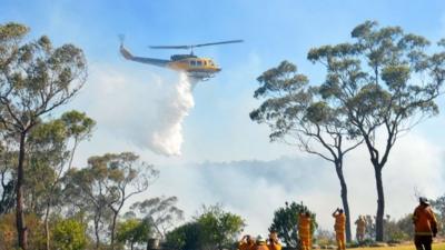 Fire fighters watch a helicopter drop water near Faulconbridge in the Blue Mountains