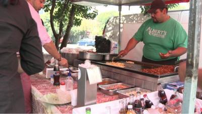 Man cooking tacos on a hot plate with bottled drinks in the foreground