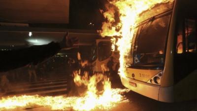 Protester gestures to bus on fire