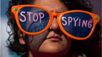 A woman wearing oversized sunglasses lettered with the words "stop spying"