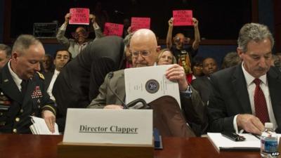 Protesters hold up placards prior to James Clapper testifying