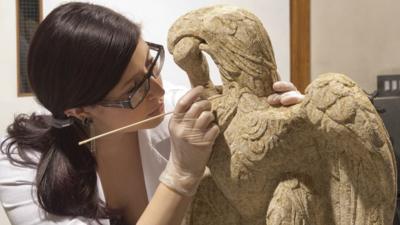 A conservator at the Museum of London Archaeology cleans a sculpture of a Minories eagle and serpent found in London