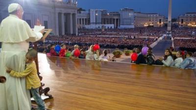 A handout picture taken on October 26, 2013 and released by Osservatore Romano on October 29, 2013 shows Pope Francis addressing the crowd at St Peter"s square in the Vatican as a boy hugs