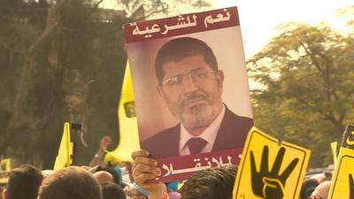 Crowds hold a President Mohammed Morsi poster