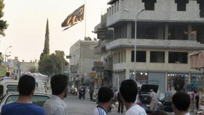 Men look at a large black flag of al-Qaeda flying in Raqqa (30 September 2013)