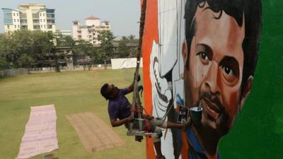 An Indian artist works on a mural of cricketer Sachin Tendulkar on the wall of a sports club building in Mumbai