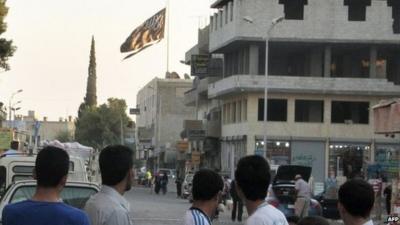 Men look at a large black flag of al-Qaeda flying in Raqqa (30 September 2013)