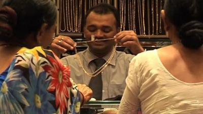 Women look at salesman's gold necklace