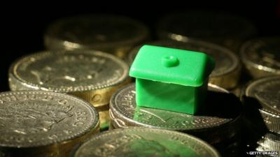 A monopoly board house resting on pound coins