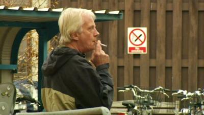 Man smoking in front of no-smoking hospital sign