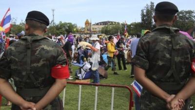 Thai soldiers, foreground, watch anti-government protesters gathering at the Royal Thai Army compound in Bangkok