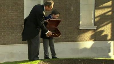 Boy pouring chest of soil into hole at site of memorial garden