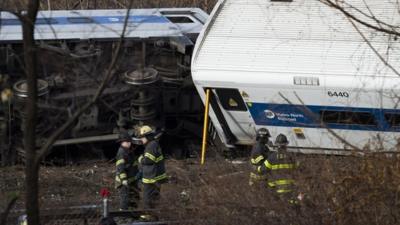 Fire fighters beside upturned Metro North Railroad train carriages