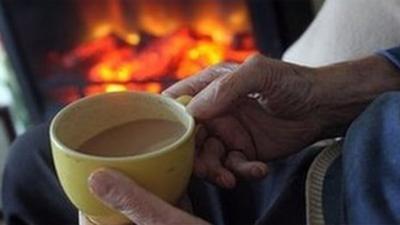 pensioner has cup of tea by the fire