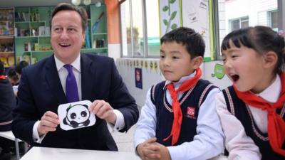 UK Prime Minister David Cameron holding a picture of a panda, with Chinese school children