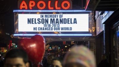 Pedestrians pass beneath the Apollo Theatre marquee commemorating the life of South African leader Nelson Mandela 5 December 2013