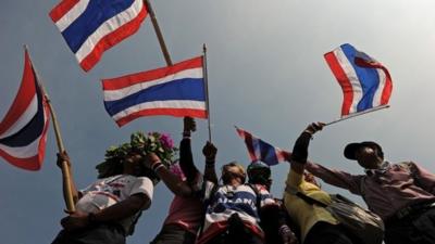 Thai anti-government protesters wave national flags as they stand on a barricade outside Government House during a rally in Bangkok on December 9, 2013