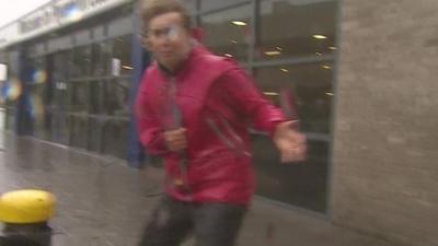 BBC reporter Sarah Ransome struggles to stay upright in high winds outside Plymouth station