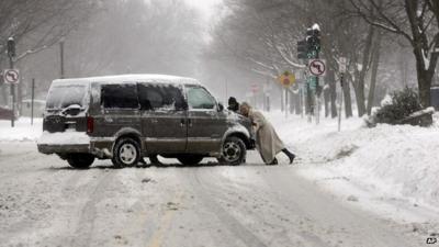 People push a car on a snowy road in Chicago on Sunday