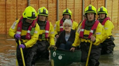 Elderly lady in canoe helped by rescue teams