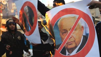 Palestinians burn a poster of former Israeli Prime Minister Ariel Sharon in the southern Gaza Strip