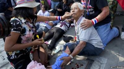 A man injured by an explosion is helped after an explosive device went off during an anti-government protest march in Bangkok on 17 January 2014