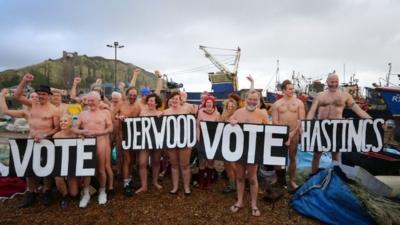 Nude people on a beach with a sign that reads "Vote Jerwood vote Hastings"