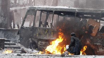 Protesters take cover behind a burnt bus during clashes in Kiev