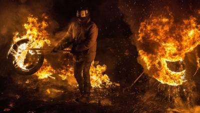 Activists of Euromaidan (the name given for Independence Square) burn tyres and warm themselves at a barricade in the center of Kiev early on January 24, 2014