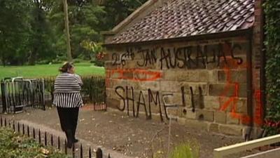 Woman loos at graffiti on side of Captain Cook's house