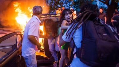 People help a family out of a burning car after it drove over a barricade of fire