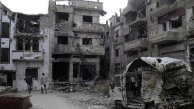 Men walk through damaged buildings in the besieged area of Homs