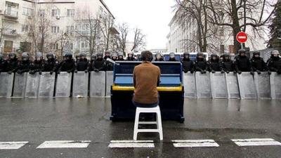 Man playing piano in front of a line of riot police