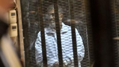 In this Tuesday, Jan. 28, 2014 photo, Egypt's ousted President Mohammed Morsi stands inside a glassed-in defendant's cage