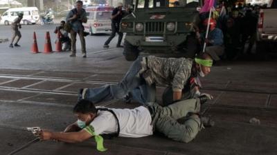 A Thai pro-election protester takes cover and aims his gun before shooting towards Thai anti-government protesters